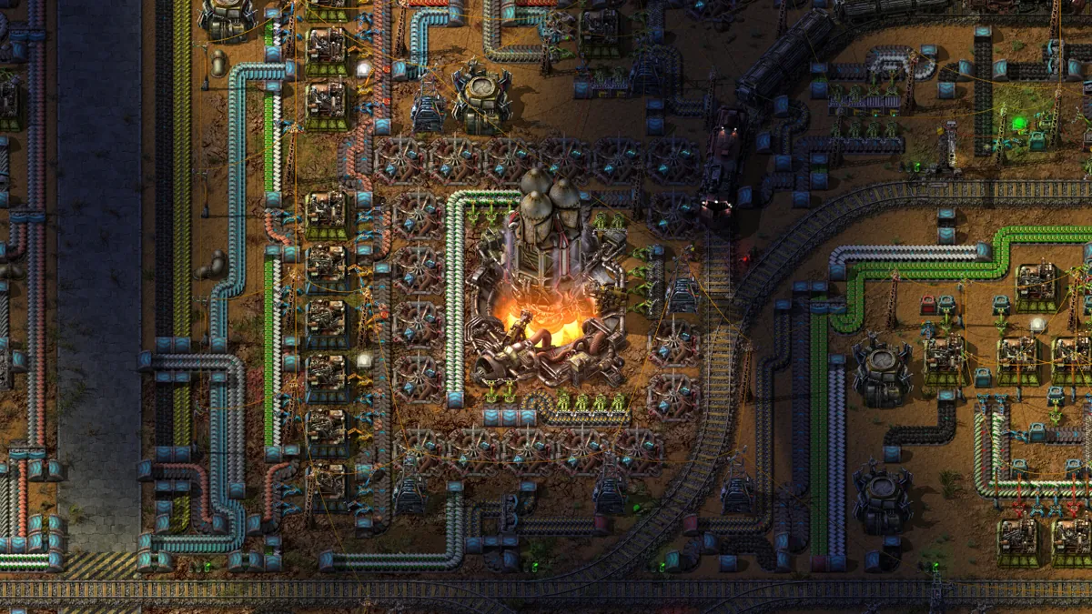 Factorioの工場。中央のロケットサイロを囲み、搬送ベルト、組立機、線路が配置されている